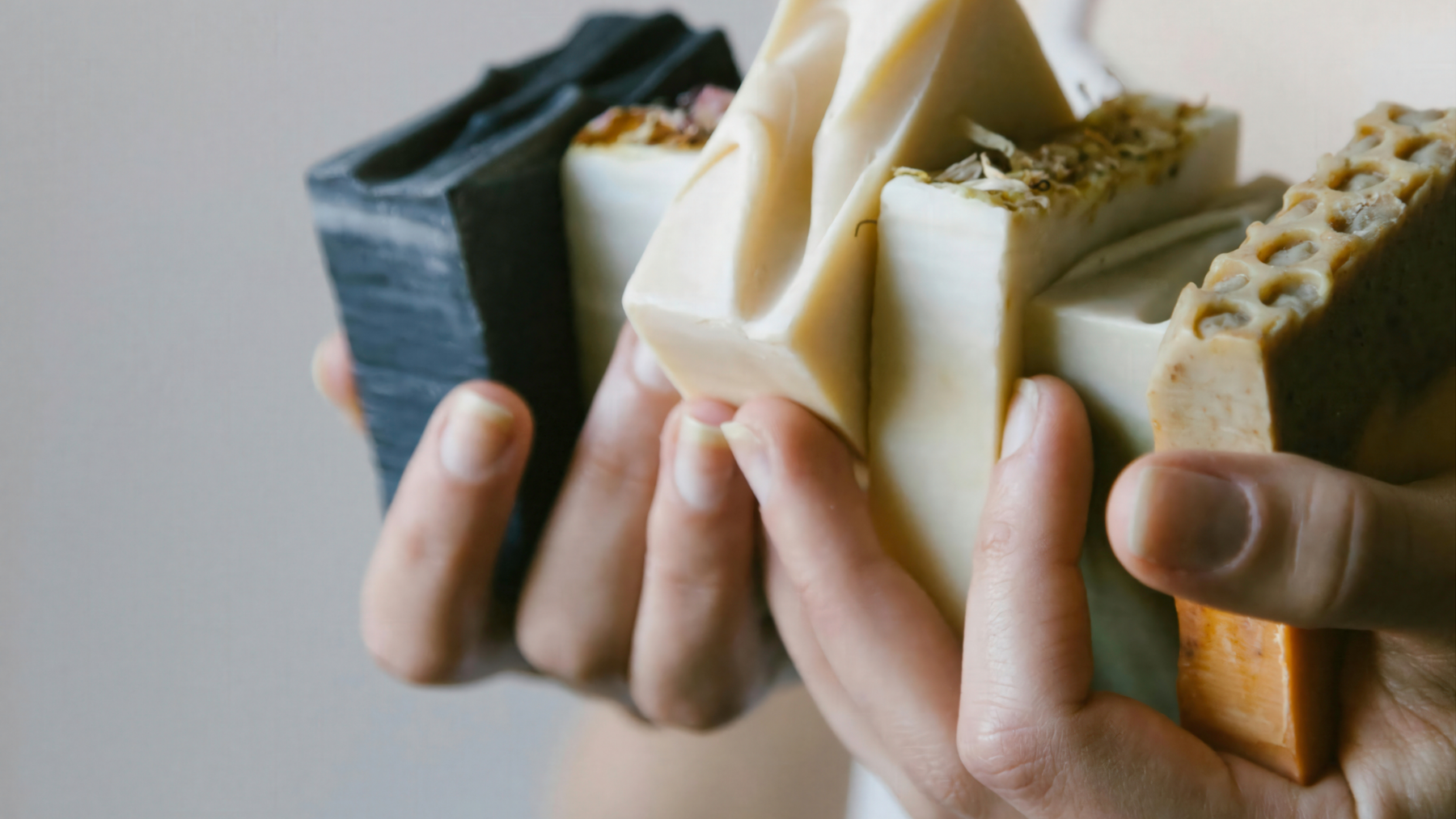 Multiple handmade natural botanical soaps being held in woman's hands.
