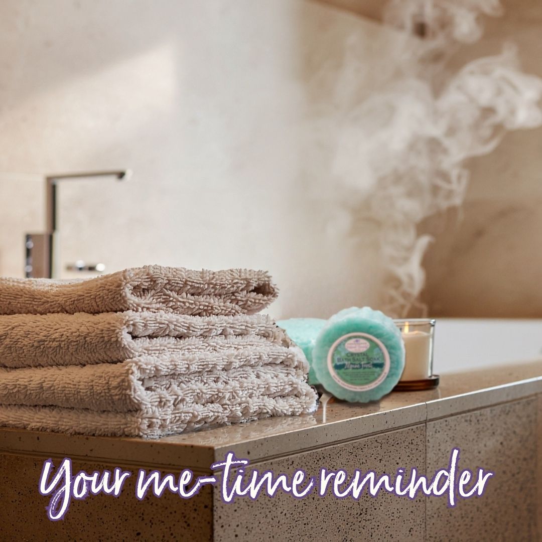 Steamy bathtub scene with Handmade Natural Beauty's Crystal Salt Soak, a candle and a stack of fluffy towels.