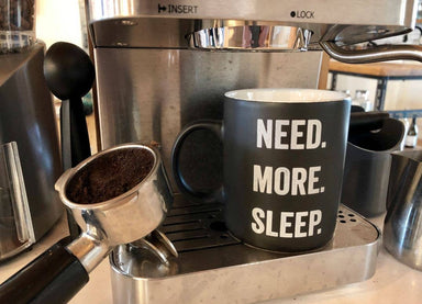 Espresso machine with a black mug labeled 'NEED. MORE. SLEEP.'