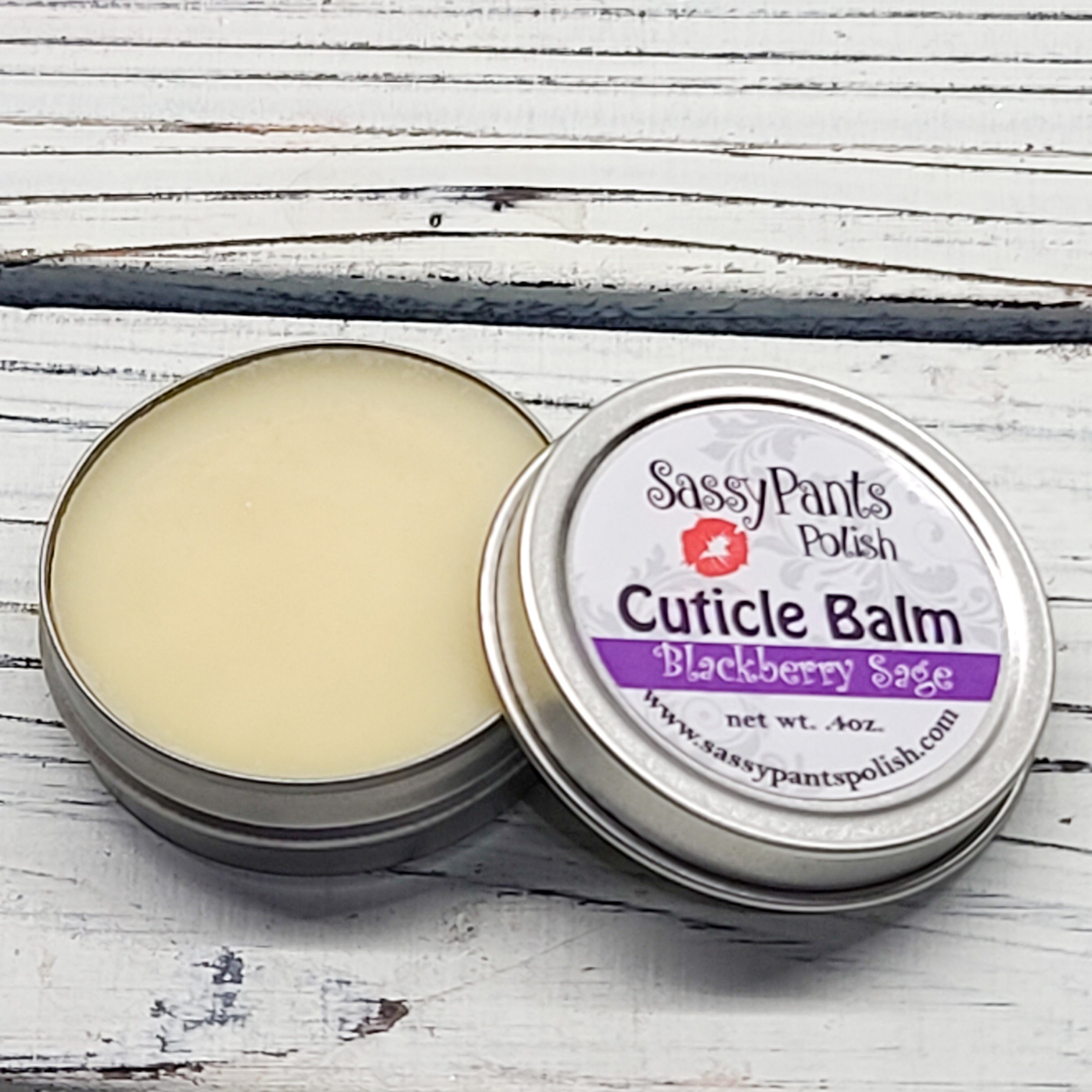 A cuticle balm open with a metal lid, showing a solid yellow cuticle balm inside, placed on a wooden surface.  Blackberry Sage