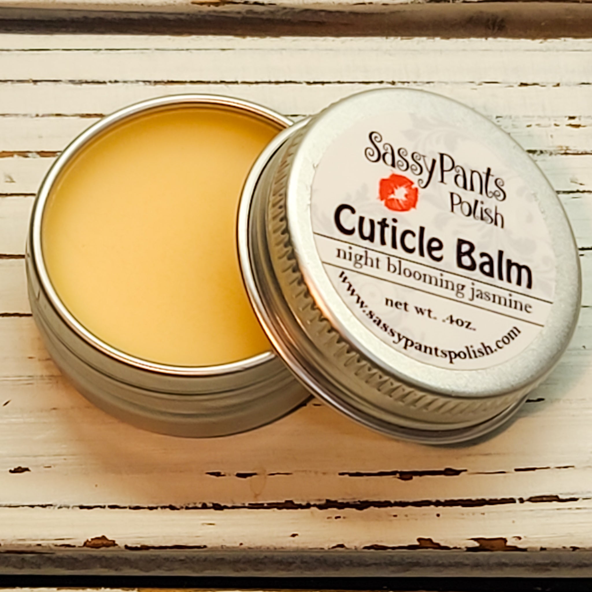 A cuticle balm open with a metal lid, showing a solid yellow cuticle balm inside, placed on a wooden surface. Night Blooming Jasmine by Sassy Pants Polish