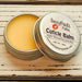 A cuticle balm open with a metal lid, showing a solid yellow cuticle balm inside, placed on a wooden surface. Night Blooming Jasmine by Sassy Pants Polish