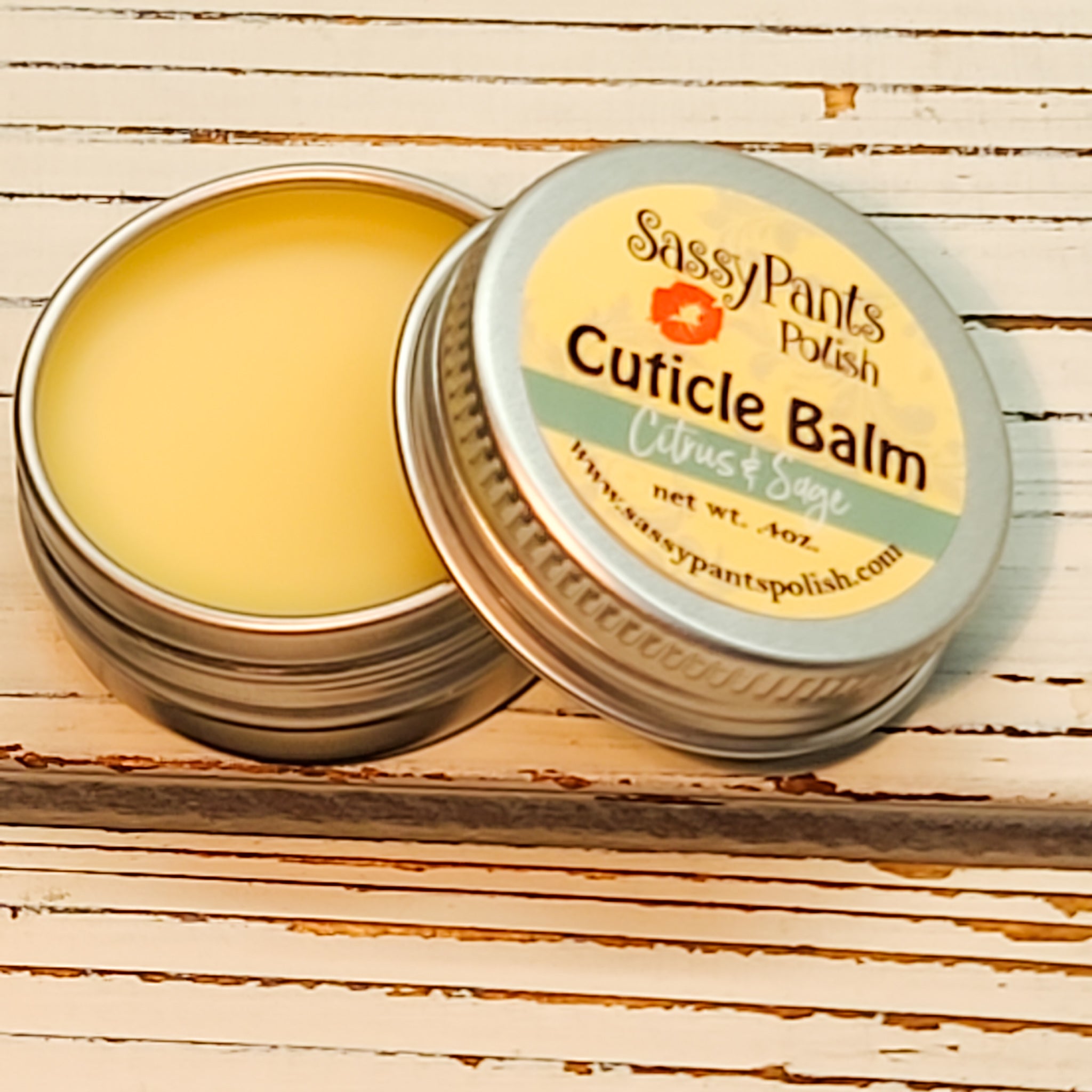 A cuticle balm open with a metal lid, showing a solid yellow cuticle balm inside, placed on a wooden surface.  Citrus & Sage by Sassy Pants Polish