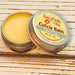 A cuticle balm open with a metal lid, showing a solid yellow cuticle balm inside, placed on a wooden surface.  Citrus & Sage by Sassy Pants Polish