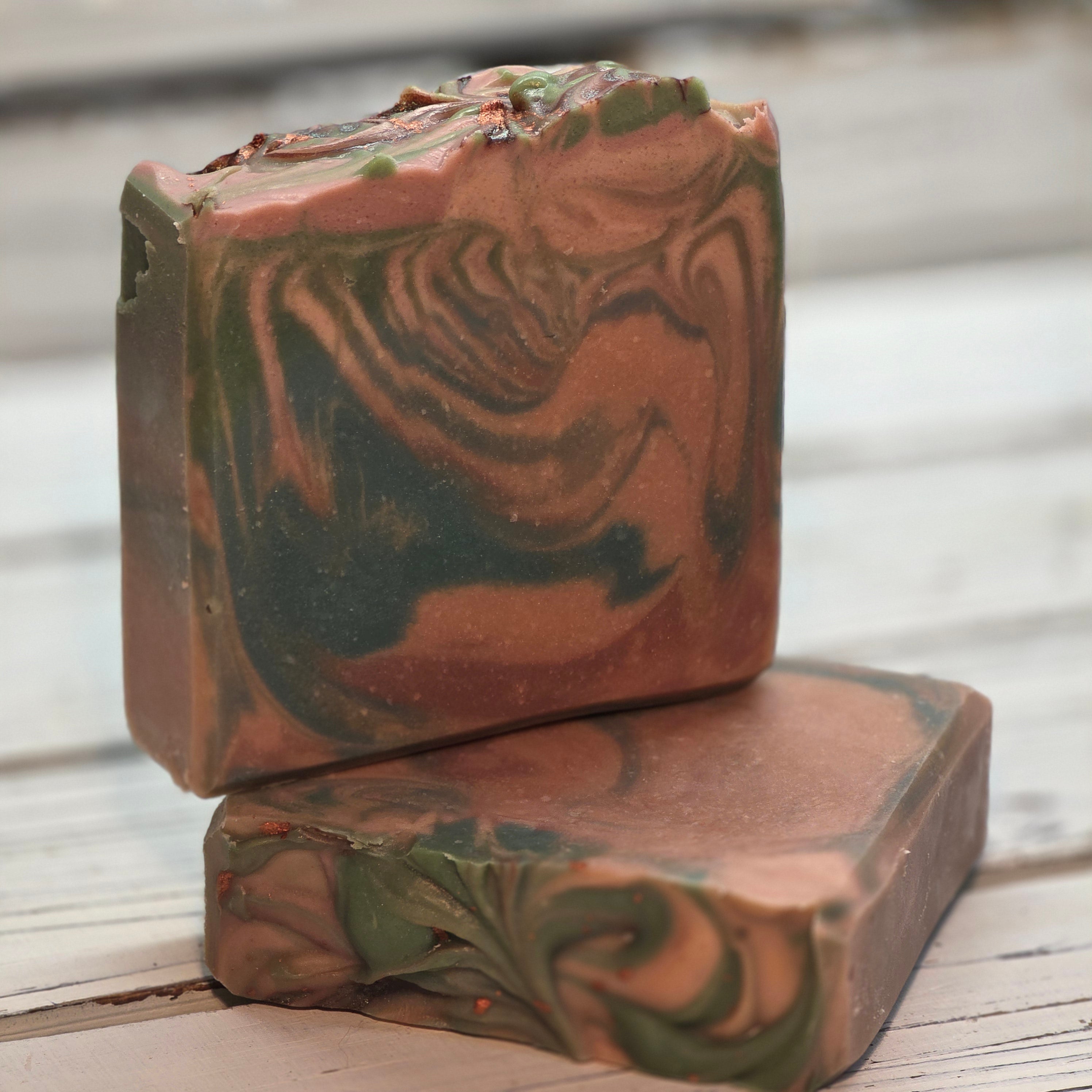 Two marbled goat milk soap soap bars with green and brown swirls on a neutral background