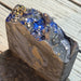 A close-up of a handmade soap bar with a rough, raw-edge top featuring a deep blue glittery interior filled with silver and gold star-shaped glitter, set against a light gray wooden background.