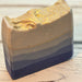 A handmade ombre blue soap bar with a gold glitter finish on top, resting on a light-colored wooden surface.
