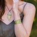 Person wearing a green floral-patterned necklace and bracelet against a blurred natural background
