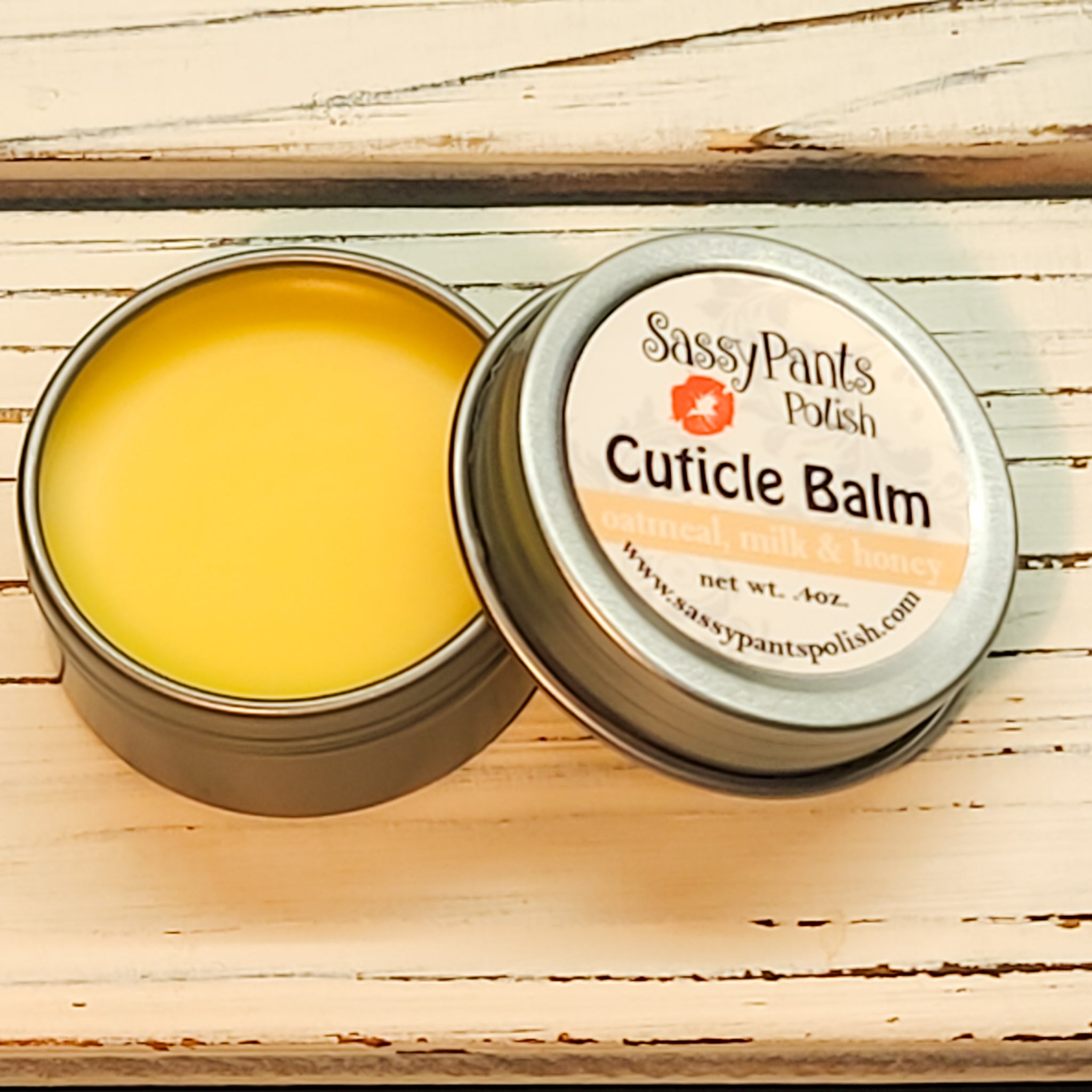 A cuticle balm open with a metal lid, showing a solid yellow cuticle balm inside, placed on a wooden surface. Oatmeal Milk & Honey
