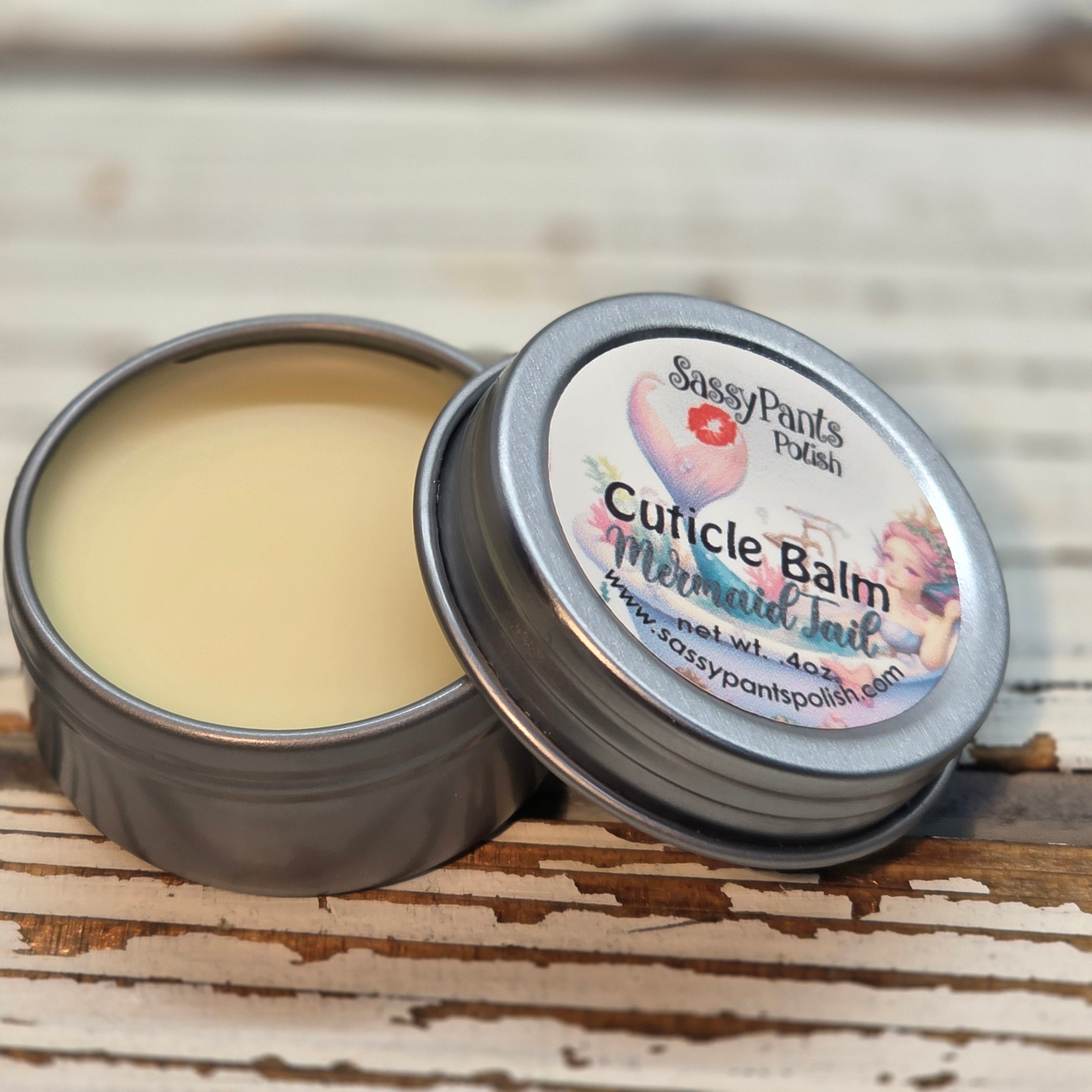 A cuticle balm open with a metal lid, showing a solid yellow cuticle balm inside, placed on a wooden surface.  Mermaid Tail by Sassy Pants Polish