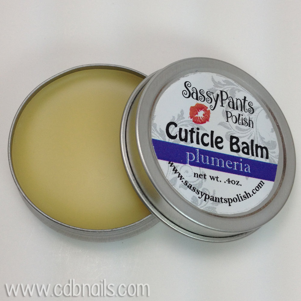 A cuticle balm open with a metal lid, showing a solid yellow cuticle balm inside, placed on a wooden surface. Plumeria by Sassy Pants Polish