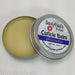 A cuticle balm open with a metal lid, showing a solid yellow cuticle balm inside, placed on a wooden surface. Plumeria by Sassy Pants Polish
