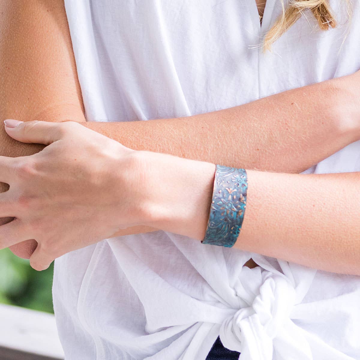 Person wearing a white shirt with a patterned bracelet on a blurred outdoor background
