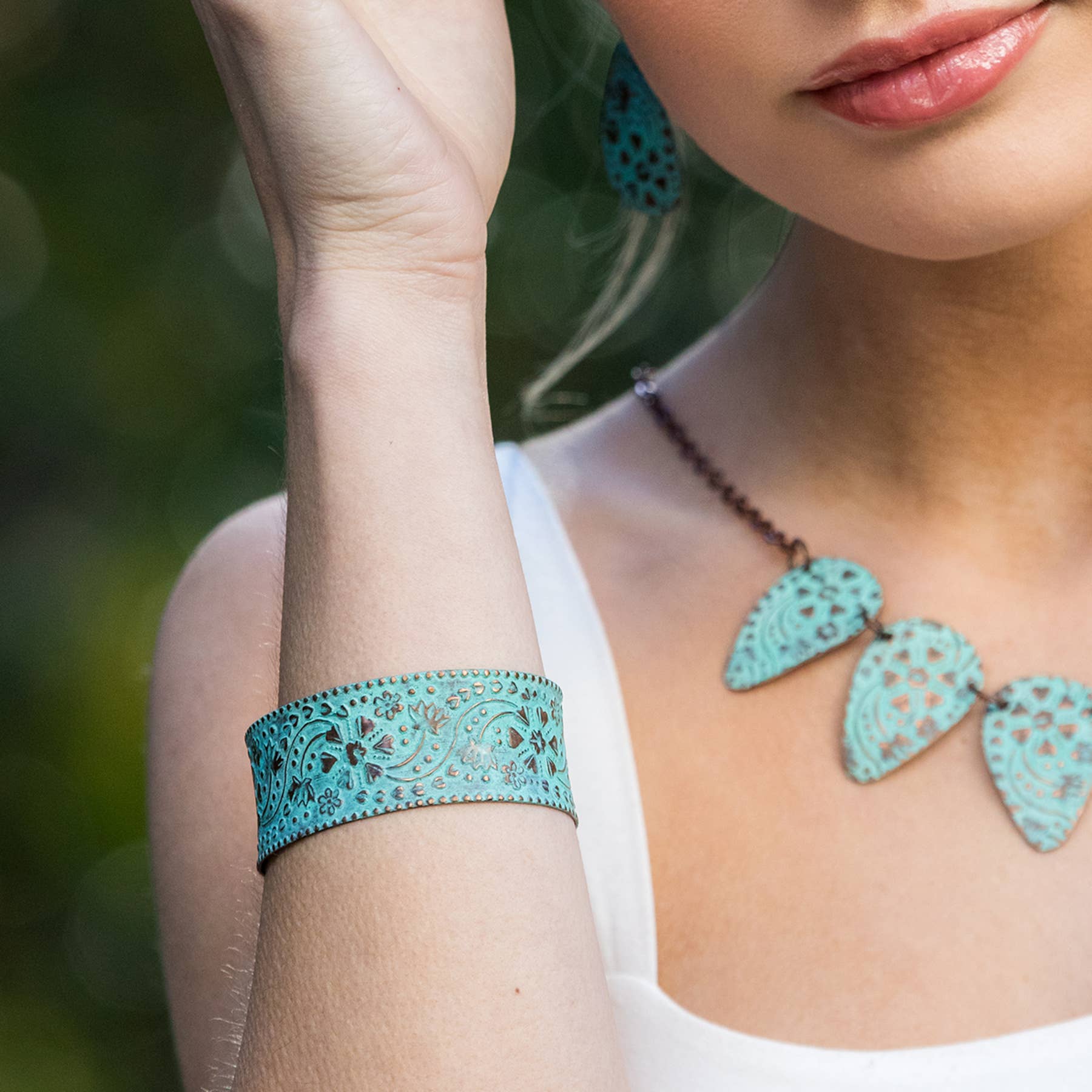 Woman wearing turquoise lace bracelet and earrings with a blurred green background