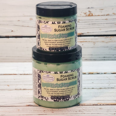 Two jars of foaming sugar scrub stacked on a wooden surface