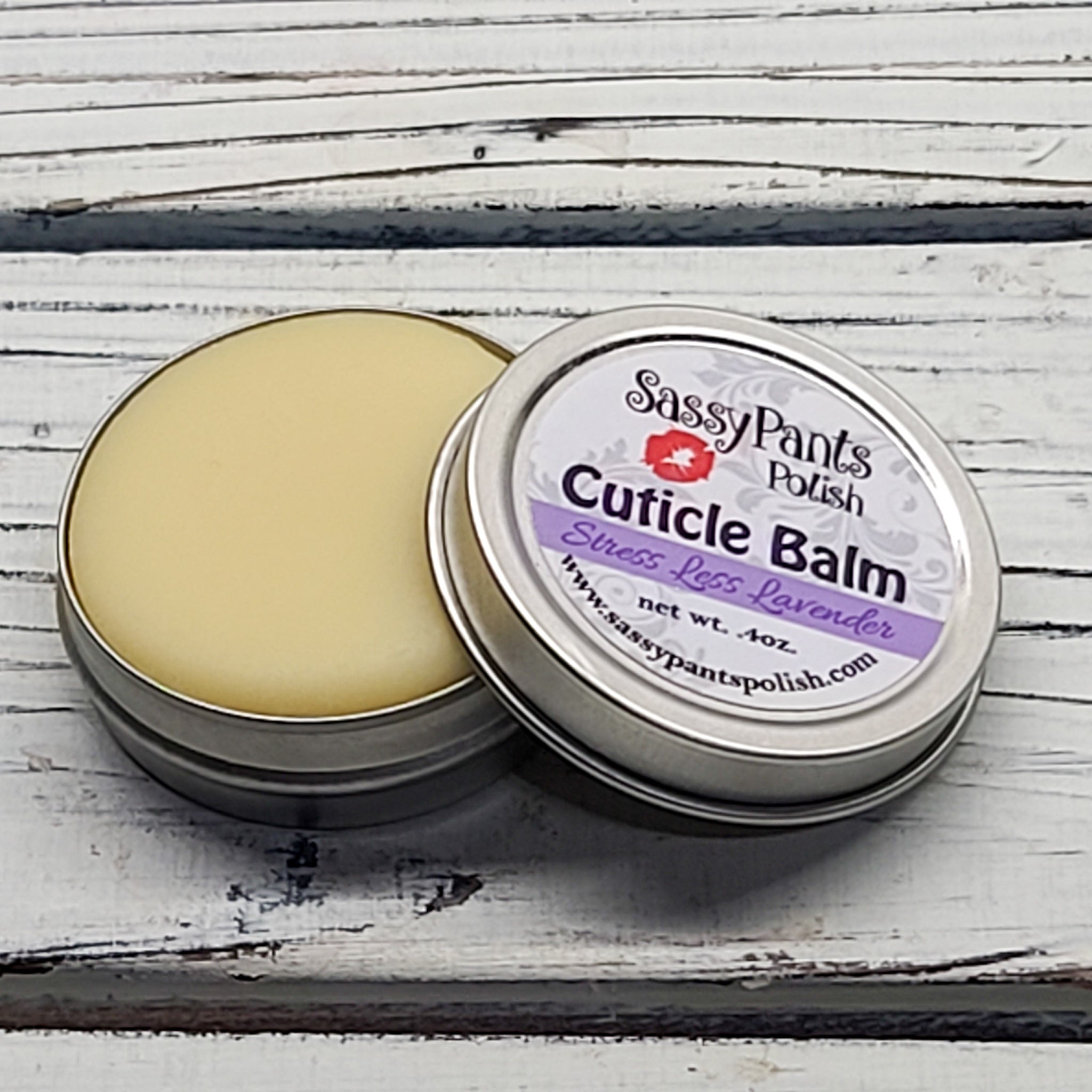 A cuticle balm open with a metal lid, showing a solid yellow cuticle balm inside, placed on a wooden surface. Stress Less Lavender