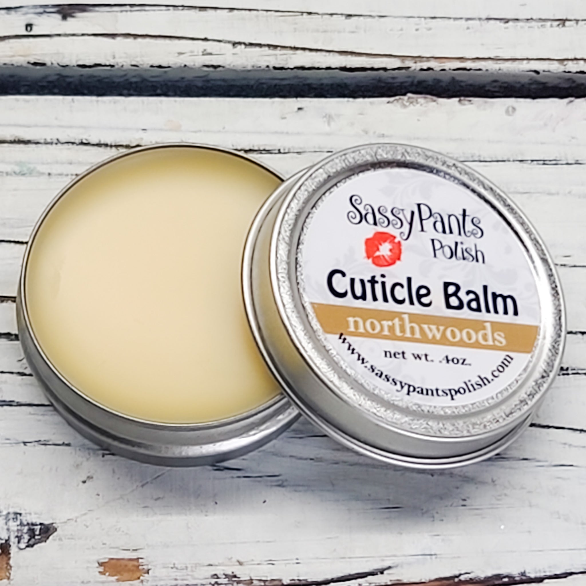 A cuticle balm open with a metal lid, showing a solid yellow cuticle balm inside, placed on a wooden surface. Northwoods