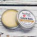 A cuticle balm open with a metal lid, showing a solid yellow cuticle balm inside, placed on a wooden surface. Northwoods