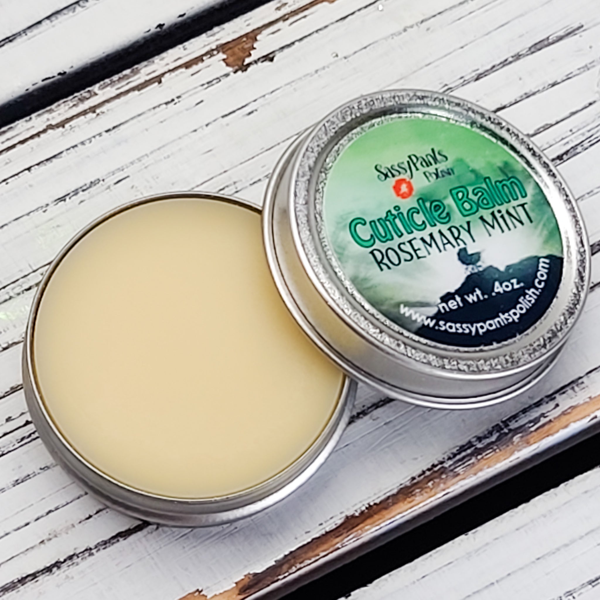 A cuticle balm open with a metal lid, showing a solid yellow cuticle balm inside, placed on a wooden surface.  Rosemary Mint