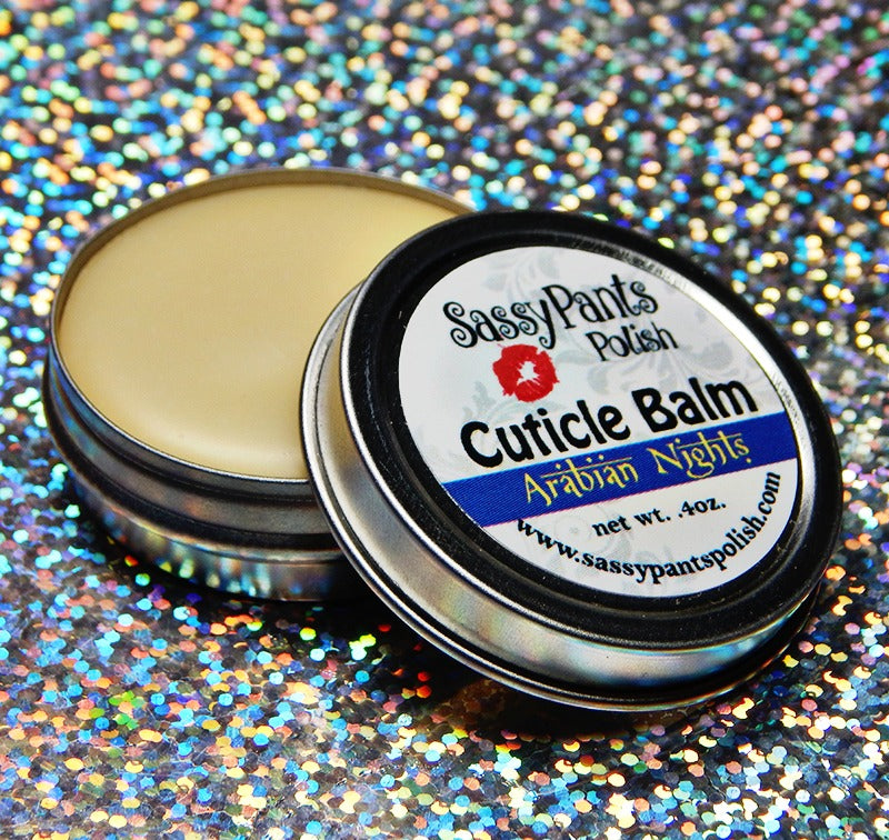 A cuticle balm open with a metal lid, showing a solid yellow cuticle balm inside, placed on a wooden surface. Arabian Nights