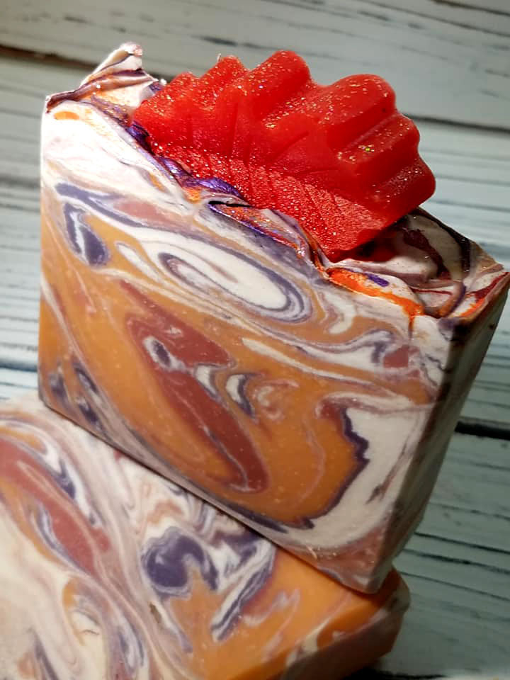 Orange purple and white swirled goat milk soap by Handmade Natural Beauty featuring various shapes of autumn leaves glycerin soaps on top.