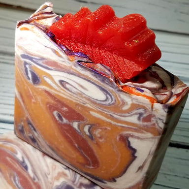 Orange purple and white swirled goat milk soap by Handmade Natural Beauty featuring an autumn leaf glycerin soap on top.