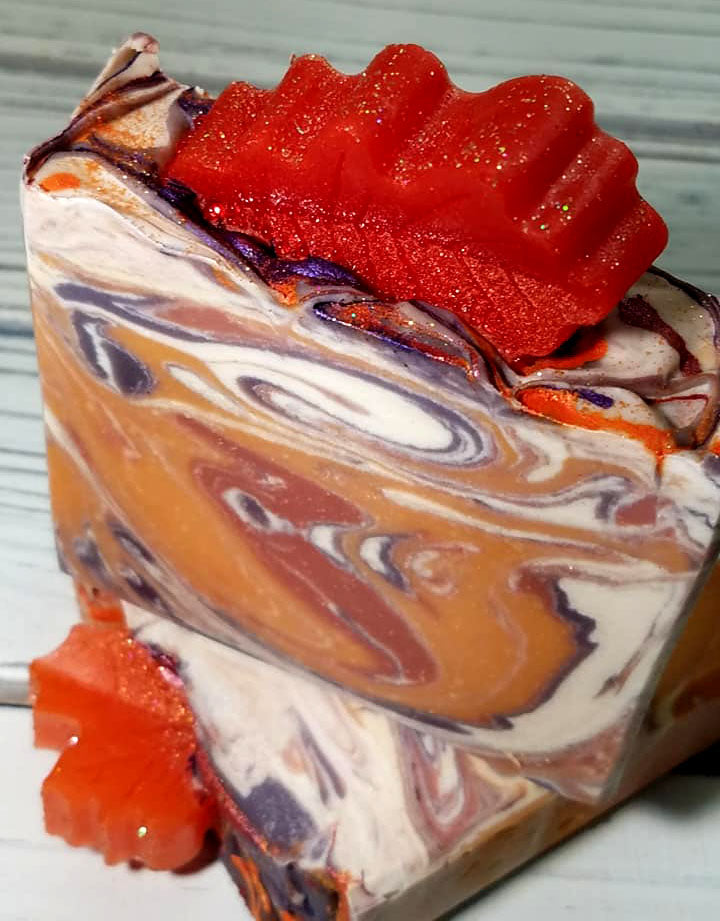 Orange purple and white swirled goat milk soap by Handmade Natural Beauty featuring various shapes of autumn leaves glycerin soaps on top.